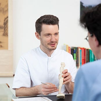 Heilpraktiker Rick Putzer bespricht beim Ersttermin mit einer Patientin an einem Akupunktur-Modell den Behandlungsablauf.