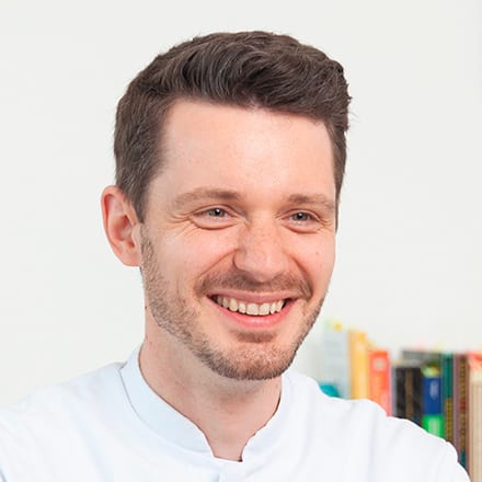 Heilpraktiker Rick Putzer in seiner Berufskleidung lächelt.