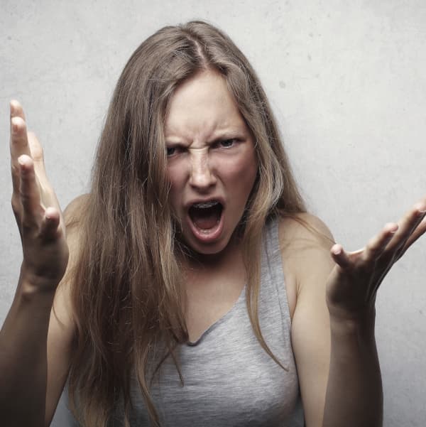 Eine Frau zeigt eine emotionale Reaktion auf Schmerz durch erhobene Arme und einen Schrei.