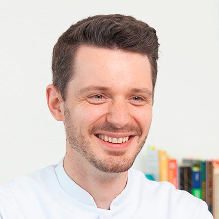 Heilpraktiker Rick Putzer in seiner Berufskleidung lächelt.