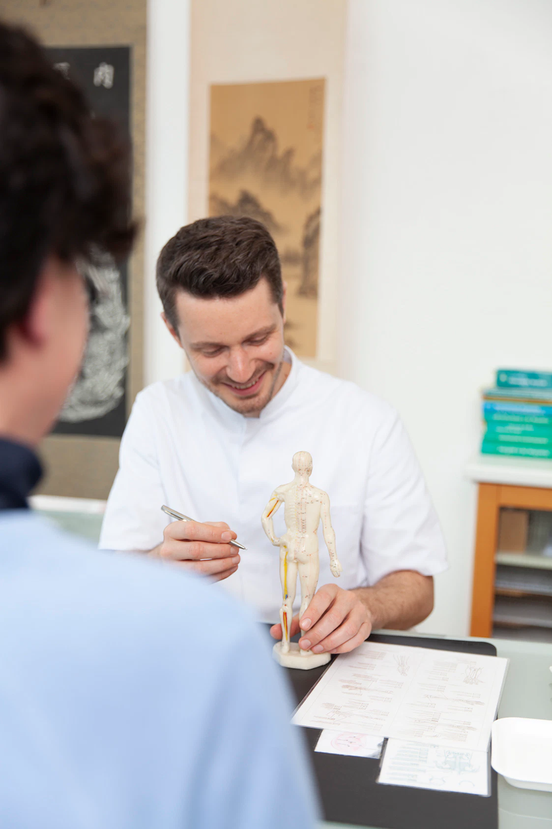 Heilpraktiker Rick Putzer erklaert Patientin die Leitbahnentherapie anhand der Akupunkturfigur.