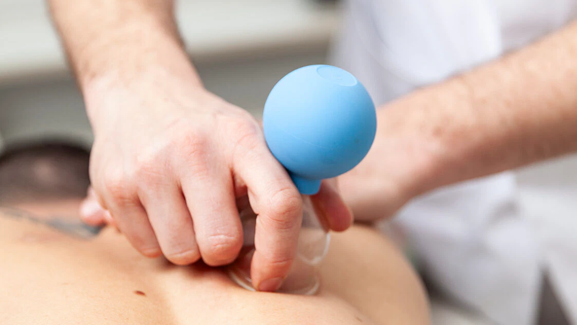 Heilpraktiker Rick Putzer massiert mit einem Schröpfkopf die Muskulatur im Bereich der Brustwirbelsäule.