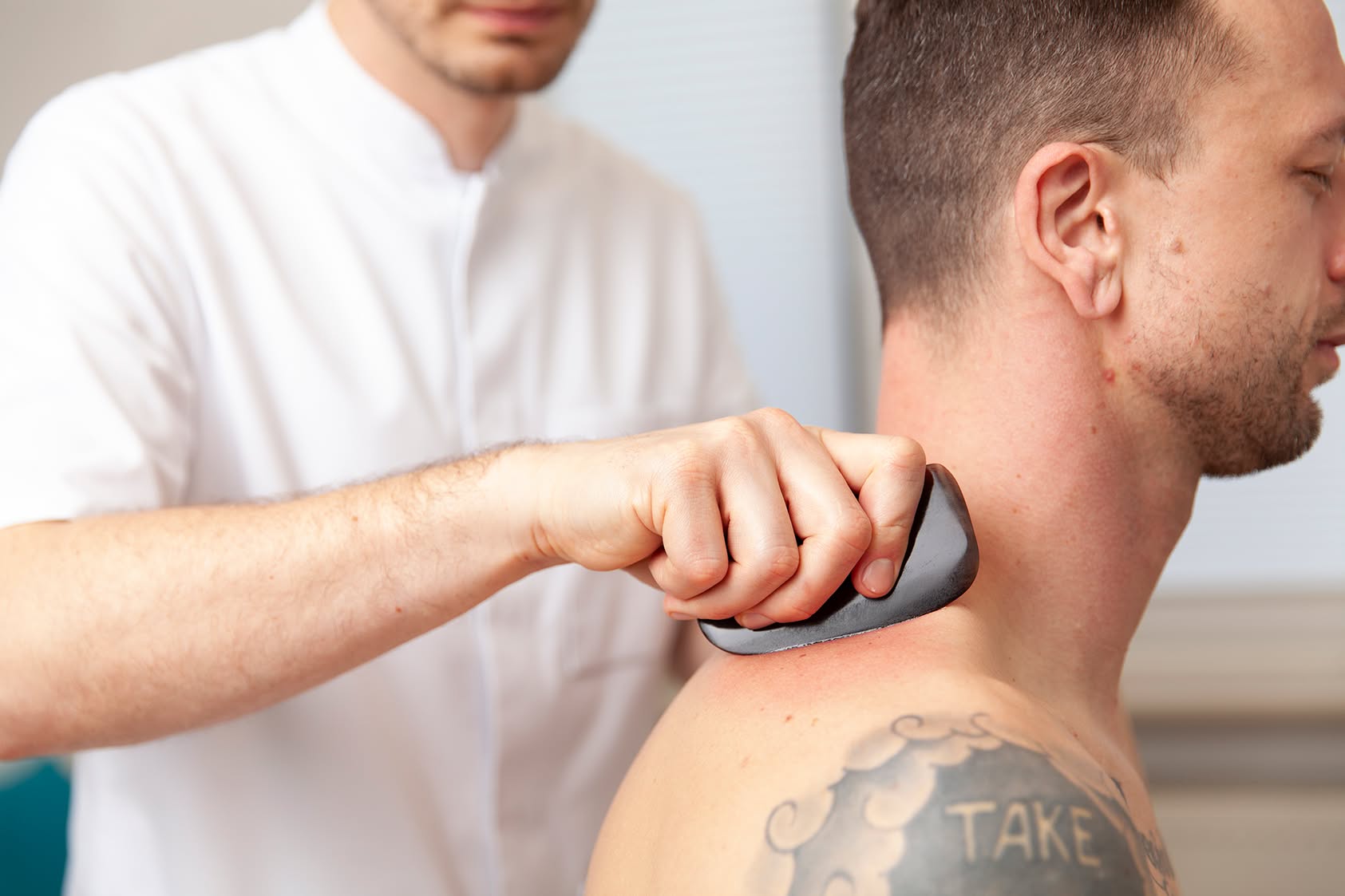 Heilpraktiker Rick Putzer führt eine Gua-Sha-Behandlung am Nacken eines Patienten durch.